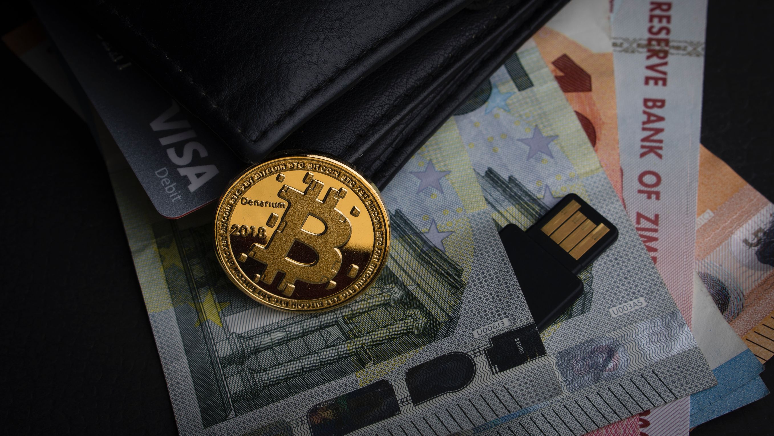 Bitcoin next to wallet with Visa card, euro notes, and other currency -- UBDI